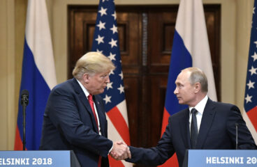 Rueda de prensa de la cumbre Estados Unidos-Rusia en Helsinki (2018). A la izquierda, Donald Trump, con traje azul, camisa blanca y corbata roja, estrecha la mano de Vladímir Putin, a la derecha, con traje negro, camisa blanca y corbata negra con lunares. En primer plano, dos atriles con el texto "Helsinki 2018". Al fondo, las banderas de Estados Unidos (rojo, blanco y azul) y Rusia (blanco, azul y rojo). Dilema estratégico de Moscú