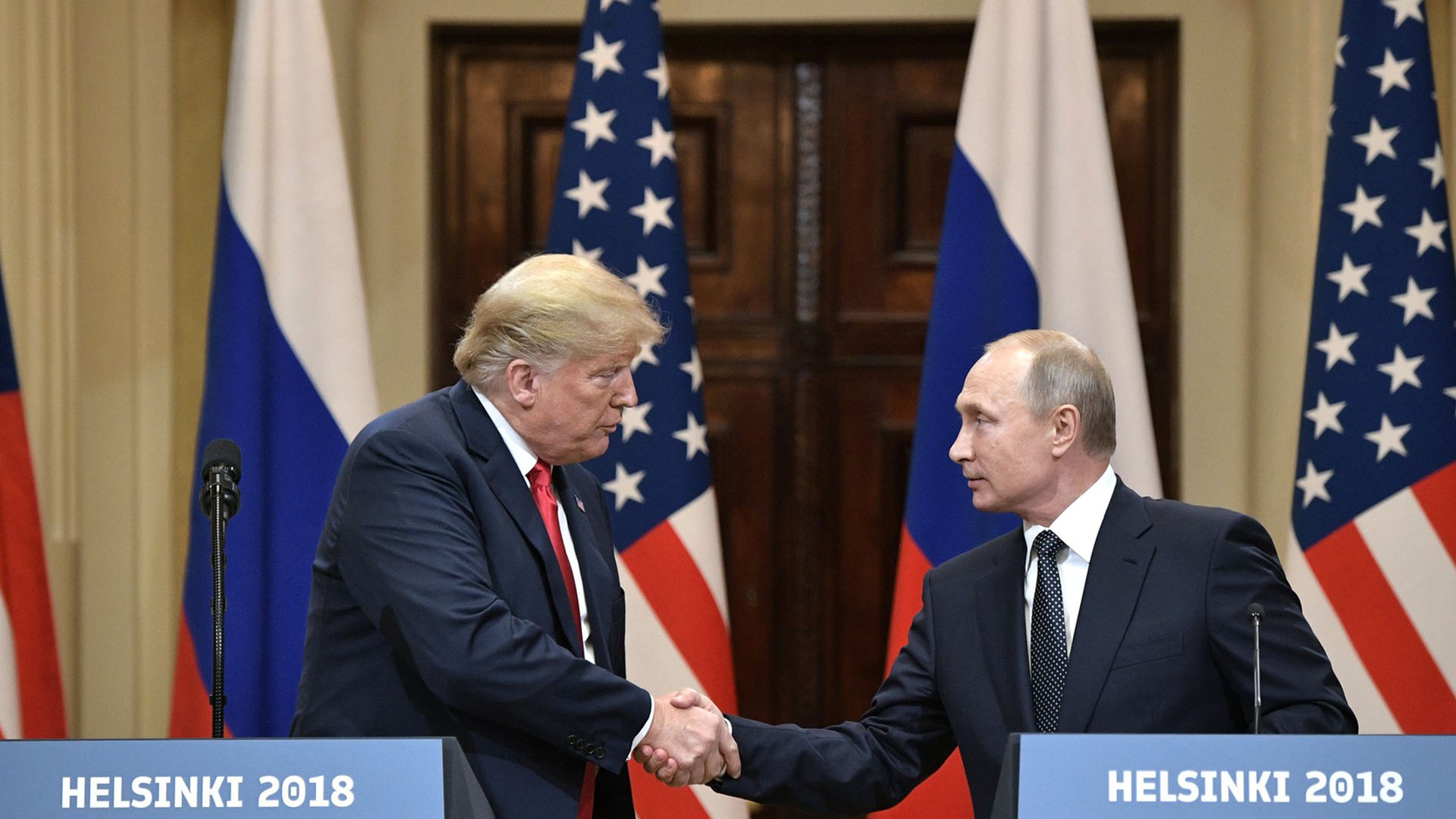 Rueda de prensa de la cumbre Estados Unidos-Rusia en Helsinki (2018). A la izquierda, Donald Trump, con traje azul, camisa blanca y corbata roja, estrecha la mano de Vladímir Putin, a la derecha, con traje negro, camisa blanca y corbata negra con lunares. En primer plano, dos atriles con el texto "Helsinki 2018". Al fondo, las banderas de Estados Unidos (rojo, blanco y azul) y Rusia (blanco, azul y rojo). Dilema estratégico de Moscú