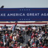 Seguidores de Donald Trump en un mitin diurno de campaña 'Make America Great Again' en el aeropuerto de Phoenix Goodyear, Arizona (EEUU). En primer plano, un cartel azul con el lema 'Make America Great Again' (Hagamos a América grande de nuevo) en letras blancas; al fondo, partes de aviones. Victoria de Trump