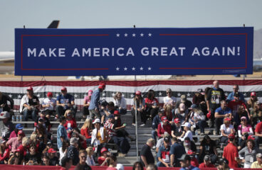 Seguidores de Donald Trump en un mitin diurno de campaña 'Make America Great Again' en el aeropuerto de Phoenix Goodyear, Arizona (EEUU). En primer plano, un cartel azul con el lema 'Make America Great Again' (Hagamos a América grande de nuevo) en letras blancas; al fondo, partes de aviones. Victoria de Trump