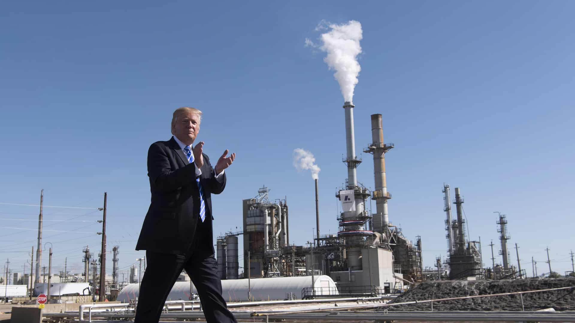 Donald Trump camina aplaudiendo frente a la refinería Andeavor en Mandan, Dakota del Norte (EEUU), con chimeneas liberando vapor o humo al fondo, en un día despejado. Trump