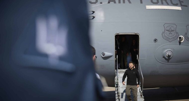 Volodímir Zelenski, presidente de Ucrania, con vestimenta oscura desciende las escaleras de un avión militar estadounidense con la inscripción "U.S. Air Force. Una figura desenfocada aparece en primer plano. Ucrania