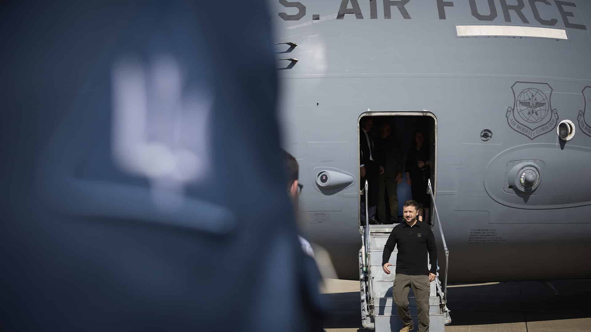 Volodímir Zelenski, presidente de Ucrania, con vestimenta oscura desciende las escaleras de un avión militar estadounidense con la inscripción "U.S. Air Force. Una figura desenfocada aparece en primer plano. Ucrania