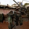 Primer plano de un edificio destruido en el Líbano, con escombros y ropa militar colgada. En el fondo, personas inspeccionan los datos sobre el techo a la luz de un día nublado. Líbano