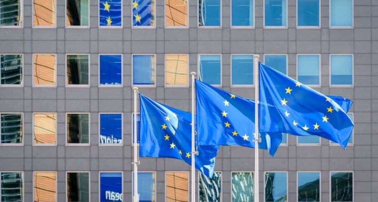 Three European Union (EU) flags fly in the wind at full mast outside the windows of the Berlaymont building, the headquarters of the European Commission (the EU executive) in Brussels, Belgium