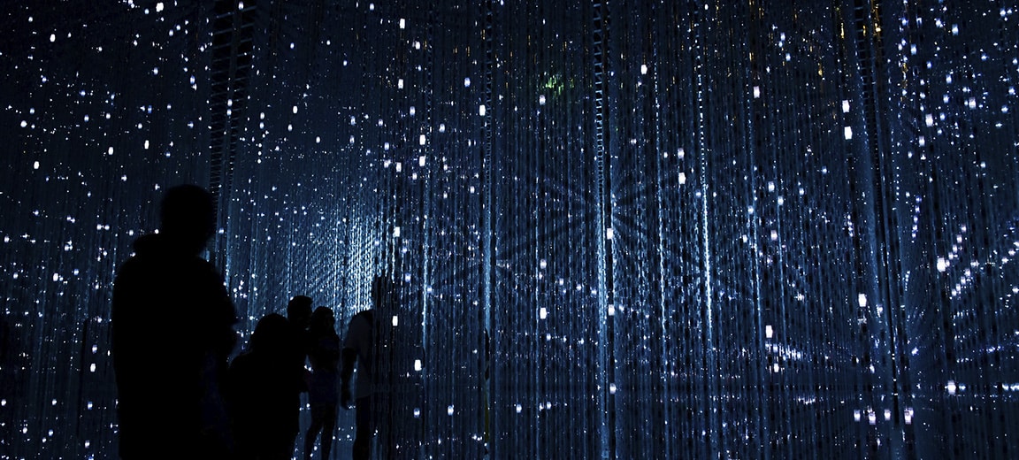 Silhouettes of people observing an interactive art installation with bright LED lights in a dark setting. Digital priorities