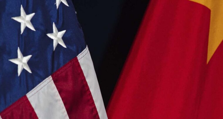 Primer plano de las banderas de Estados Unidos y China, parcialmente visibles sobre un fondo oscuro. La bandera de Estados Unidos muestra estrellas blancas sobre azul y franjas rojas y blancas, mientras la de China presenta fondo rojo con una estrella amarilla. Geopolítica