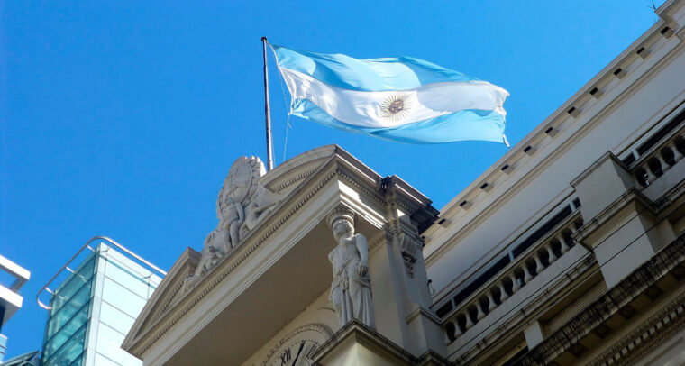 Low view of the façade of the building of the Central Bank of the Argentine Republic with a blue and white Argentine flag flying under a clear sky. Stabilisation plan