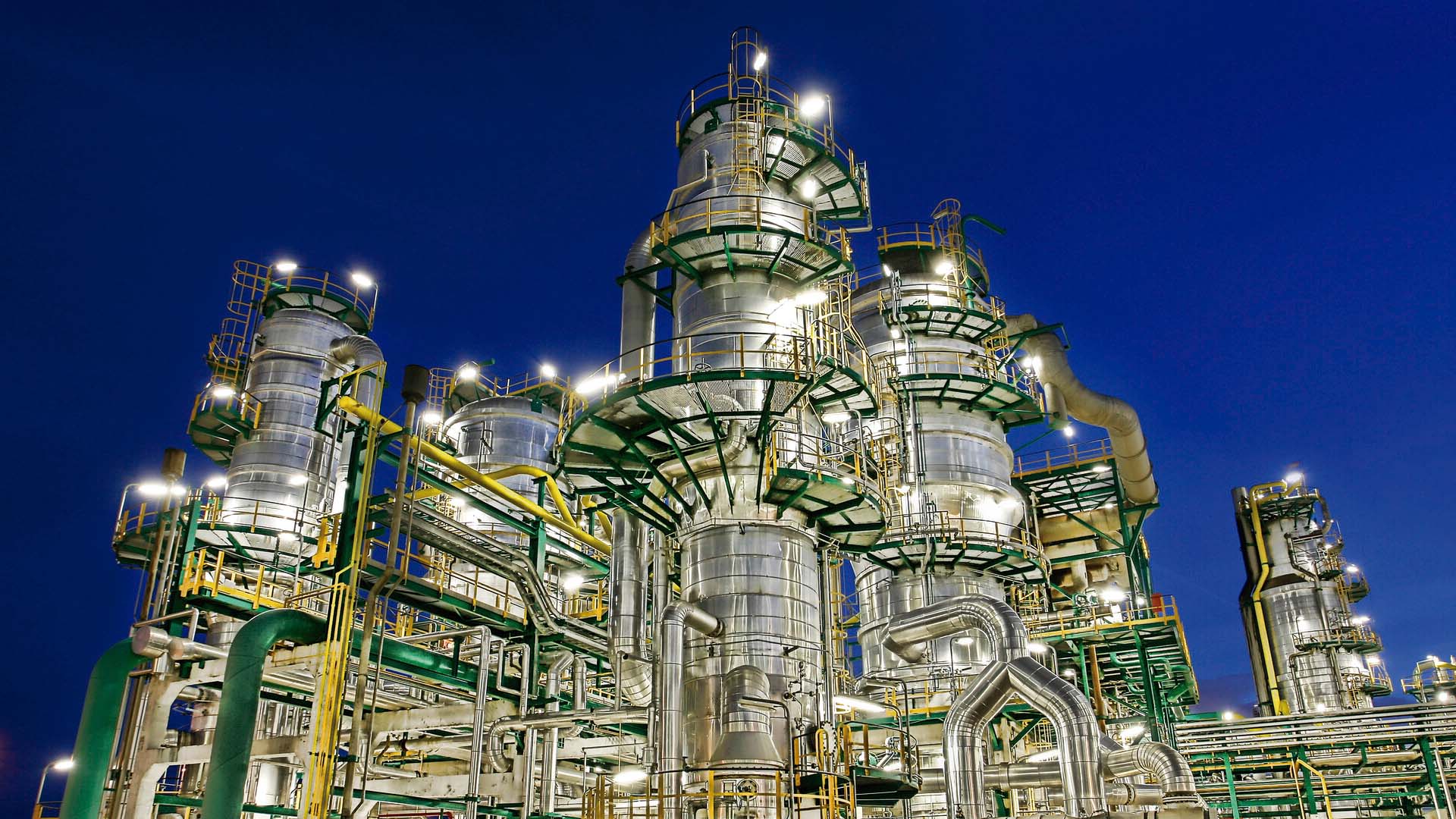 Petrochemical complex located in Tarragona illuminated at night, with large industrial structures, pipelines and platforms framed by a dark blue sky.