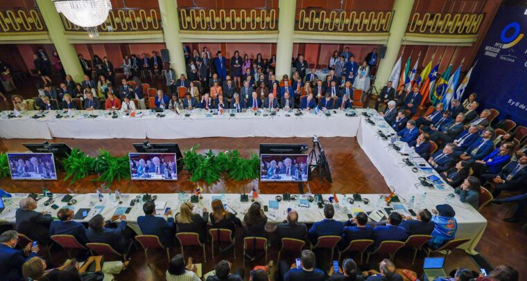 Detail of the Summit of Presidents of the Member States and Associate States of MERCOSUR in Montevideo (Uruguay), where participants are seated around a large conference table in a formal room, with the flags of MERCOSUR countries in the background, on 6 December 2024. EU-Mercosur