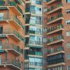 A close-up view of a residential brick apartment building with multiple balconies and green railings. Economy