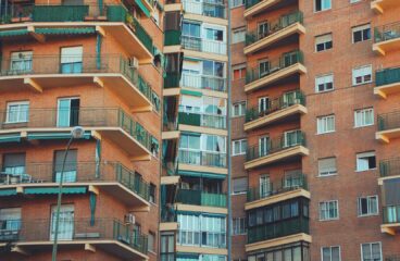 A close-up view of a residential brick apartment building with multiple balconies and green railings. Economy