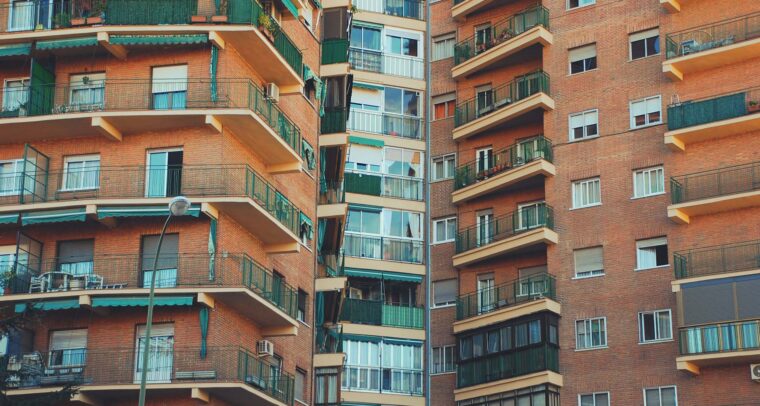 A close-up view of a residential brick apartment building with multiple balconies and green railings. Economy