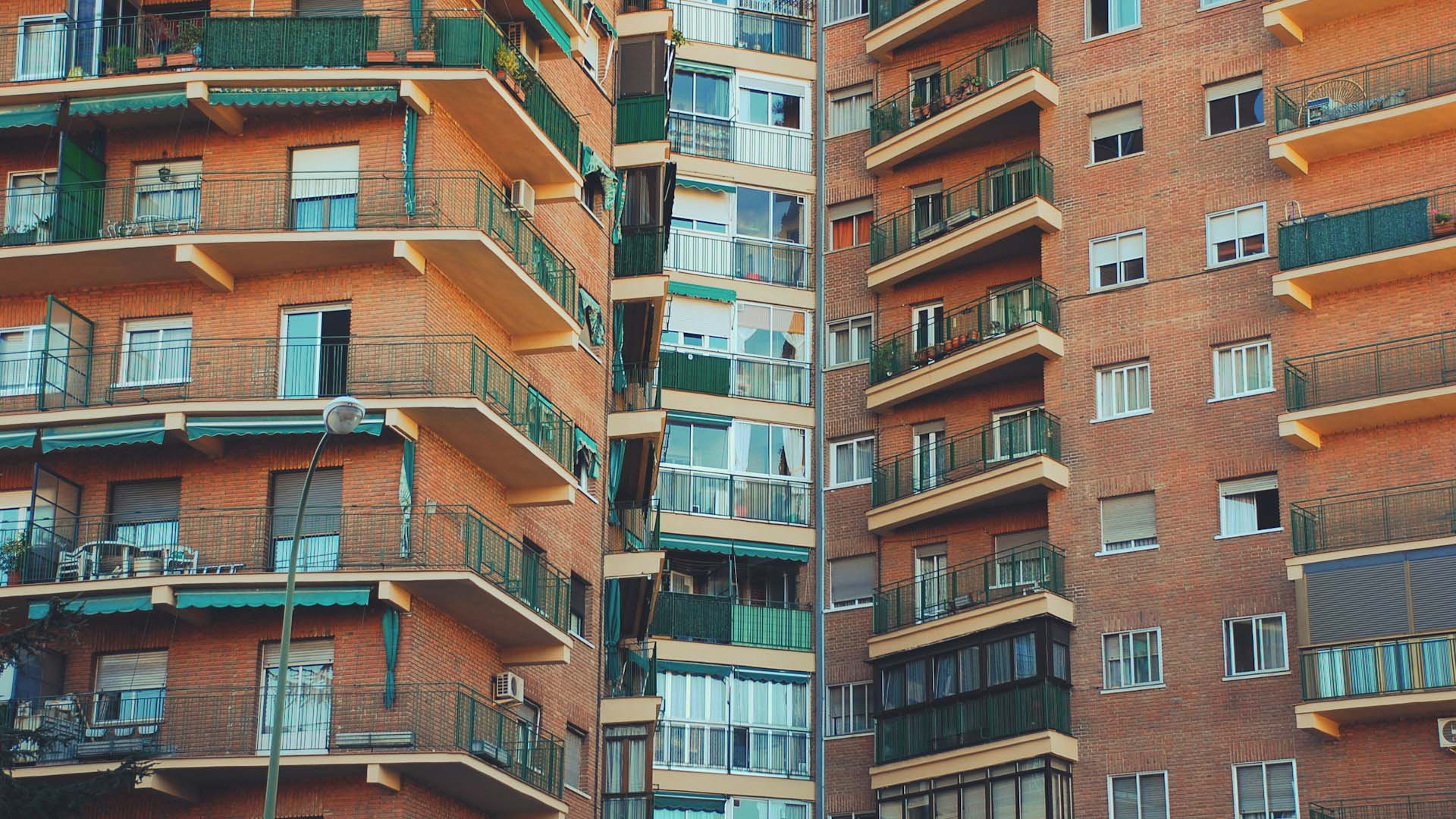 A close-up view of a residential brick apartment building with multiple balconies and green railings. Economy