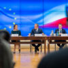 Reunión oficial de la Conferencia de Presidentes del Parlamento Europeo con el primer ministro polaco Donald Tusk y representantes del gobierno de Polonia. En el fondo, se observa una pantalla con la bandera de la Unión Europea y la bandera de Polonia, mientras los participantes dialogan en torno a una mesa en un entorno institucional. Presidencia