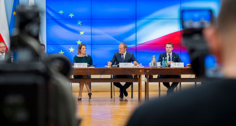 Reunión oficial de la Conferencia de Presidentes del Parlamento Europeo con el primer ministro polaco Donald Tusk y representantes del gobierno de Polonia. En el fondo, se observa una pantalla con la bandera de la Unión Europea y la bandera de Polonia, mientras los participantes dialogan en torno a una mesa en un entorno institucional. Presidencia