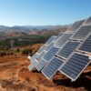 A series of solar panels installed on a hillside near the city of Ovalle (Chile) set against a rural landscape with distant mountains under the clear blue sky of Monte Patria. Colombia and Chile