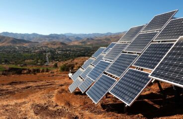 A series of solar panels installed on a hillside near the city of Ovalle (Chile) set against a rural landscape with distant mountains under the clear blue sky of Monte Patria. Colombia and Chile