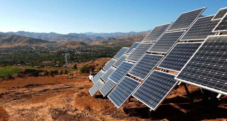 A series of solar panels installed on a hillside near the city of Ovalle (Chile) set against a rural landscape with distant mountains under the clear blue sky of Monte Patria. Colombia and Chile