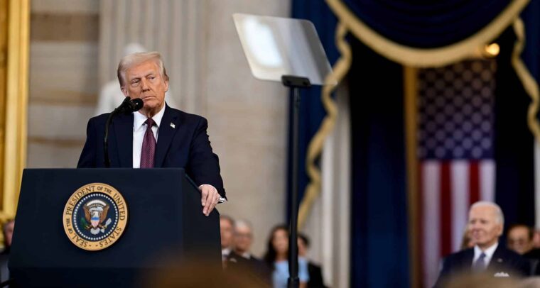 Donald Trump pronuncia un discurso durante su ceremonia de investidura como presidente de los Estados Unidos, en Washington, el 20 de enero de 2025. Está de pie detrás de un atril con el escudo presidencial. Lleva un traje azul marino, una camisa blanca y una corbata roja oscura. Al fondo, se aprecia una bandera de los Estados Unidos. Asimismo, se percibe, de forma desenfocada, la figura de Joe Biden, expresidente de los Estados Unidos. Foto: The Trump White House (Wikimedia Commons/Dominio público). Trump