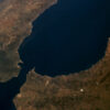 Vista aérea diurna del Estrecho de Gibraltar, separando España (norte) y Marruecos (sur). Se observan la Sierra Nevada en España, la costa montañosa de Marruecos, el río Guadalquivir y las ciudades de Gibraltar y Ceuta bajo cielos despejados. Ceuta y Melilla