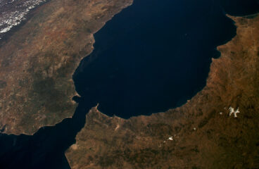 Vista aérea diurna del Estrecho de Gibraltar, separando España (norte) y Marruecos (sur). Se observan la Sierra Nevada en España, la costa montañosa de Marruecos, el río Guadalquivir y las ciudades de Gibraltar y Ceuta bajo cielos despejados. Ceuta y Melilla