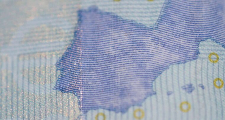 Detalle de un billete de 20 euros, con líneas azules finas, una parte del mapa de Europa y detalles dorados. Se aprecian la textura del papel y el brillo parcial de la tinta. Inversiones