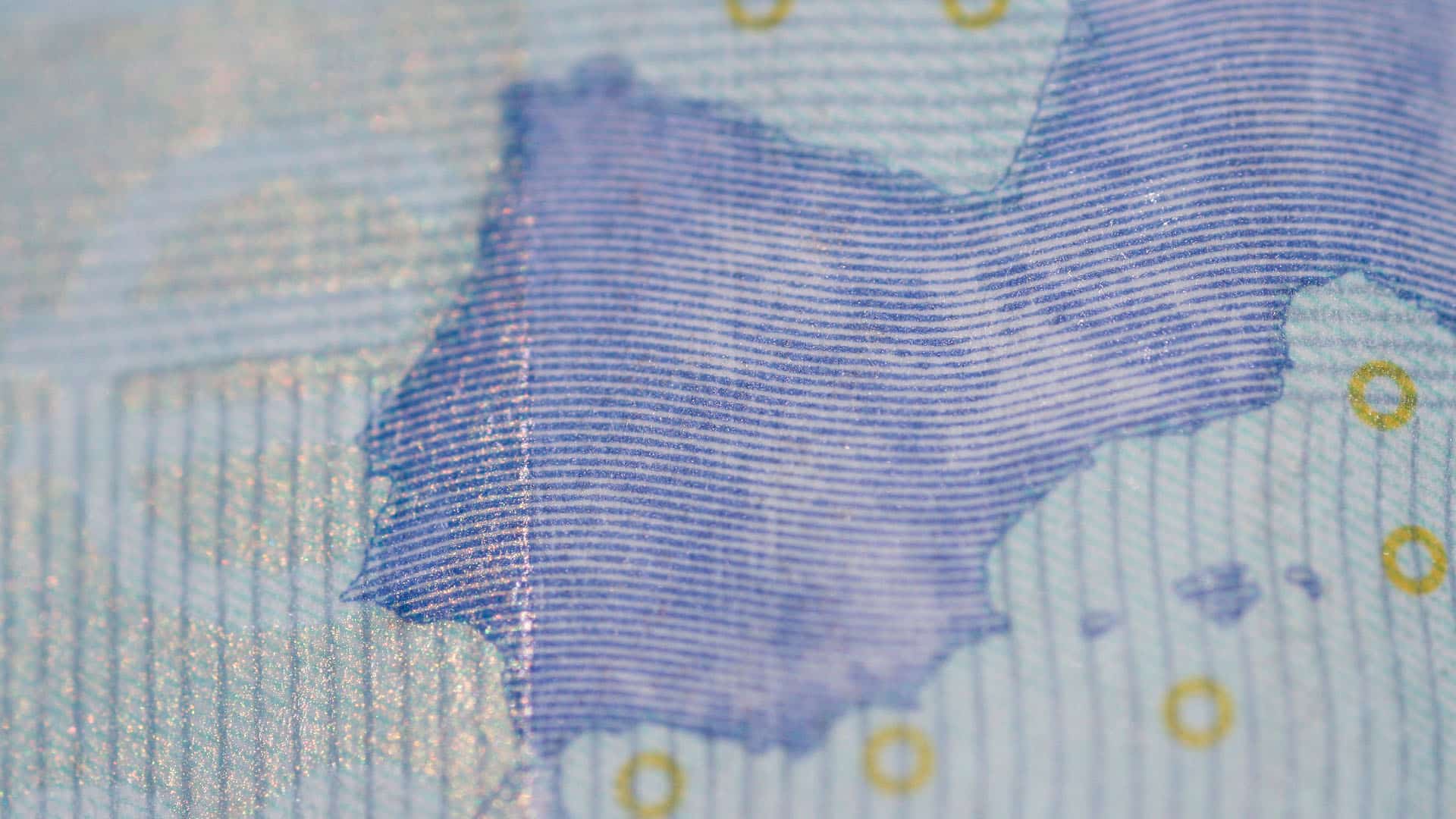 Detalle de un billete de 20 euros, con líneas azules finas, una parte del mapa de Europa y detalles dorados. Se aprecian la textura del papel y el brillo parcial de la tinta. Inversiones