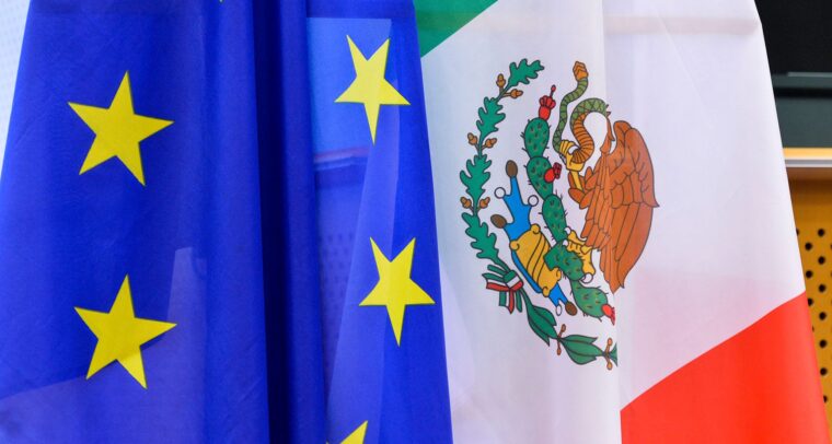 Flags of the European Union (blue with a circle of yellow stars) and Mexico (tricolour with green, white, and red stripes, featuring a coat of arms with an eagle and a serpent) at the 25th Meeting of the Mexico-European Union Joint Parliamentary Committee in 2018. Mexico