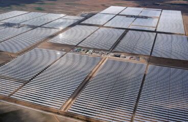 Vista aérea de una gran planta de energía solar térmica situada en la provincia de Granada (España). En primer plano, se muestran extensas filas de espejos parabólicos que reflejan la luz del sol, con una pequeña zona de infraestructura en el centro, rodeada de un paisaje árido. Draghi