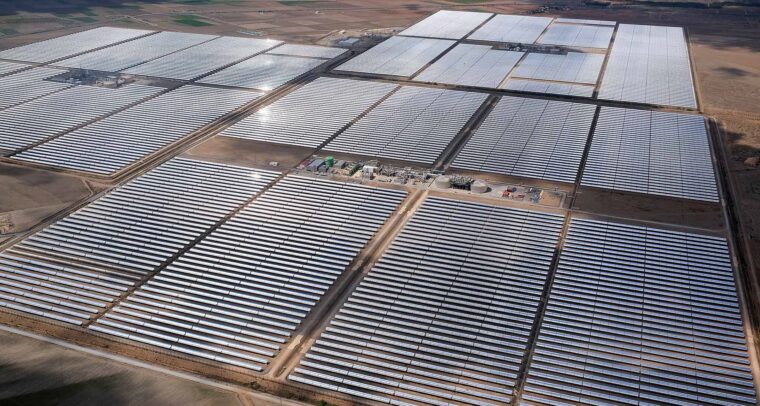 Vista aérea de una gran planta de energía solar térmica situada en la provincia de Granada (España). En primer plano, se muestran extensas filas de espejos parabólicos que reflejan la luz del sol, con una pequeña zona de infraestructura en el centro, rodeada de un paisaje árido. Draghi