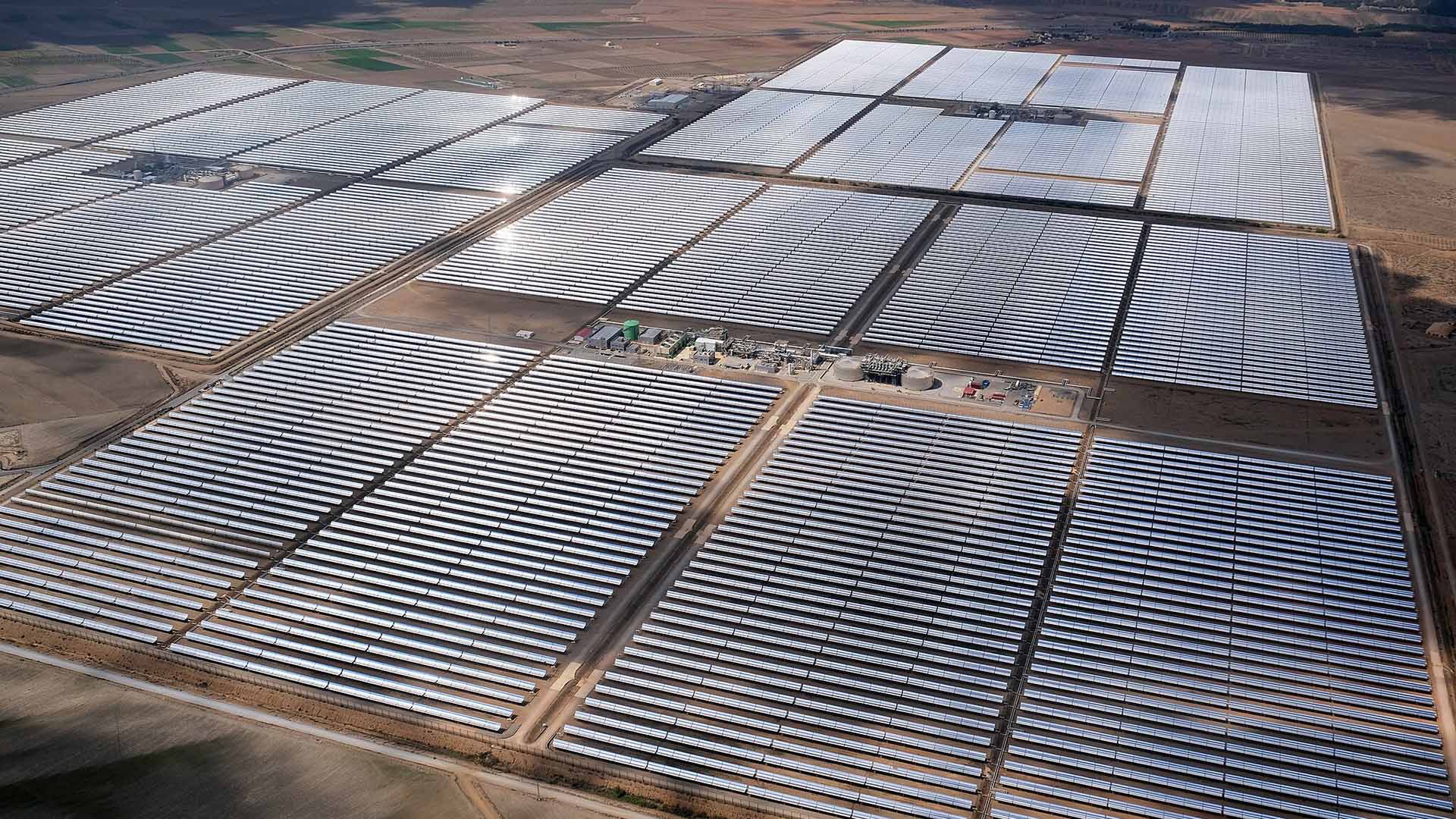 Vista aérea de una gran planta de energía solar térmica situada en la provincia de Granada (España). En primer plano, se muestran extensas filas de espejos parabólicos que reflejan la luz del sol, con una pequeña zona de infraestructura en el centro, rodeada de un paisaje árido. Draghi