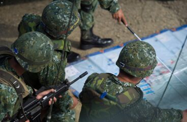 Maniobras militares durante la visita de la presidenta Tsai al condado de Pingtung (Taiwán). En primer plano, tres soldados, vestidos con uniforme militar y casco, observan un mapa. Al fondo, se distingue de forma difusa el brazo de un soldado más. Taiwán