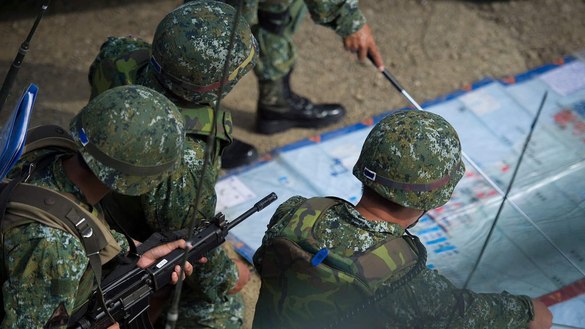 Maniobras militares durante la visita de la presidenta Tsai al condado de Pingtung (Taiwán). En primer plano, tres soldados, vestidos con uniforme militar y casco, observan un mapa. Al fondo, se distingue de forma difusa el brazo de un soldado más. Taiwán