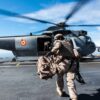 Primer plano de un soldado vestido con el uniforme militar español, con una mochila en la mano izquierda, corriendo hacia un helicóptero de la Armada Española durante operaciones anfibias desde el barco de cuatro anclas FS Mistral, como parte del ejercicio Brilliant Mariner 17, en un día soleado. Gasto de defensa