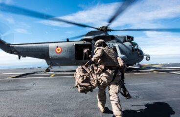 Primer plano de un soldado vestido con el uniforme militar español, con una mochila en la mano izquierda, corriendo hacia un helicóptero de la Armada Española durante operaciones anfibias desde el barco de cuatro anclas FS Mistral, como parte del ejercicio Brilliant Mariner 17, en un día soleado. Gasto de defensa