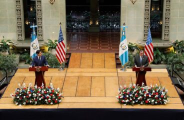 El secretario de Estado de EEUU, Marco Rubio (traje azul marino, camisa blanca y corbata azul marino con puntos blancos), y el presidente de Guatemala, Bernardo Arévalo (traje gris oscuro, camisa blanca y corbata azul cielo), durante una rueda de prensa conjunta en el Palacio Nacional de la Cultura (Ciudad de Guatemala), el 5 de febrero de 2025. Ambos están de pie detrás de podios de madera con el escudo nacional de Guatemala, sobre una tarima elevada con arreglos florales al frente. A sus lados se encuentran las banderas de Estados Unidos y Guatemala sobre soportes. De fondo, se aprecia la decoración del espacio, con arcos ornamentados y vegetación. Marco Rubio