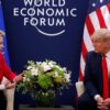 Ursula von der Leyen (chaqueta roja, camisa blanca y pantalón negro), presidenta de la Comisión Europea, y Donald Trump (traje azul marino, corbata roja y camisa blanca), presidente de Estados Unidos, se reúnen durante el Foro Económico Mundial en Davos en 2020. Ambos están sentados en unos sillones color crema, con una mesa de café entre ellos, presidida por un arreglo de flores blancas y verdes. Detrás, sobre un fondo azul oscuro, se lee ‘World Economic Forum’, con las banderas de la UE y de Estados Unidos situadas a los lados. Aranceles de Trump