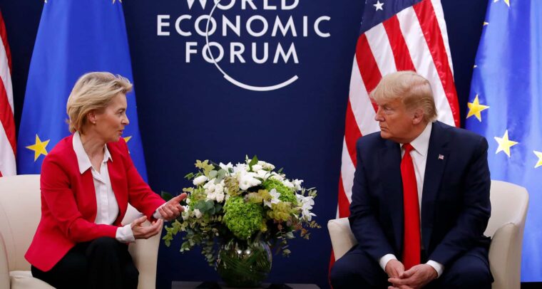 Ursula von der Leyen (chaqueta roja, camisa blanca y pantalón negro), presidenta de la Comisión Europea, y Donald Trump (traje azul marino, corbata roja y camisa blanca), presidente de Estados Unidos, se reúnen durante el Foro Económico Mundial en Davos en 2020. Ambos están sentados en unos sillones color crema, con una mesa de café entre ellos, presidida por un arreglo de flores blancas y verdes. Detrás, sobre un fondo azul oscuro, se lee ‘World Economic Forum’, con las banderas de la UE y de Estados Unidos situadas a los lados. Aranceles de Trump