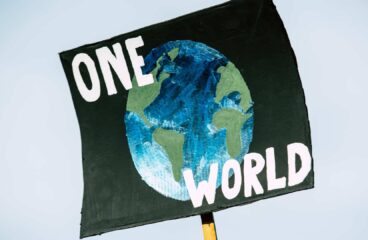 Hand-painted poster for the global climate change protest demonstration strike. On a black background, the representation of a globe in shades of green and blue with the words ‘One World’