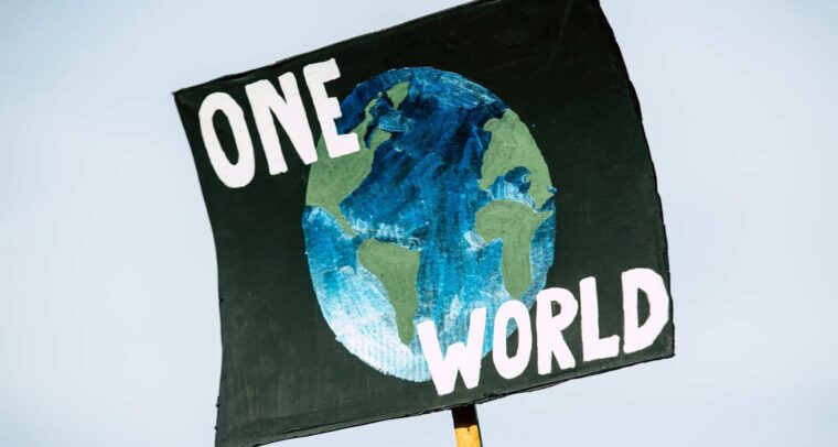 Hand-painted poster for the global climate change protest demonstration strike. On a black background, the representation of a globe in shades of green and blue with the words ‘One World’