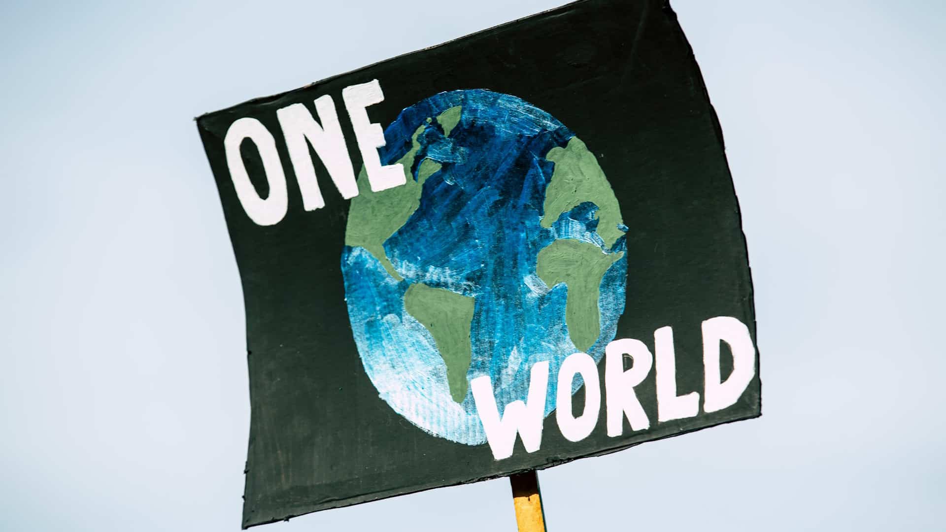 Hand-painted poster for the global climate change protest demonstration strike. On a black background, the representation of a globe in shades of green and blue with the words ‘One World’