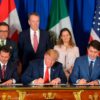 En primer plano, de izquierda a derecha, se encuentran sentados y firmando el tratado de libre comercio entre EEUU, Canadá y México (USMCA) en la cumbre del G20 en Argentina en el año 2018: Enrique Peña Nieto, expresidente de México, con un traje negro, camisa blanca y corbata a rayas rojas y azules; Donald Trump, presidente de EEUU, con un traje azul oscuro, camisa blanca y corbata roja; y Justin Trudeau, primer ministro de Canadá, con un traje, camisa y corbata en distintas tonalidades de azul. Al fondo, se vislumbran las banderas de Estados Unidos, Canadá y México, así como tres personas que acompañan la firma (dos hombres y una mujer de pie), con un fondo azul. Trump