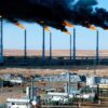 Hassi R’Mel, el mayor campo y hub de gas en Argelia, con múltiples antorchas de gas quemando y emitiendo humo negro sobre una vasta instalación industrial en el desierto. Gas