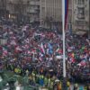 Multitud de manifestantes marchando en Belgrado (Serbia), con banderas y pancartas en protesta contra la corrupción gubernamental, mientras la policía y personal de seguridad supervisan el evento. Serbia