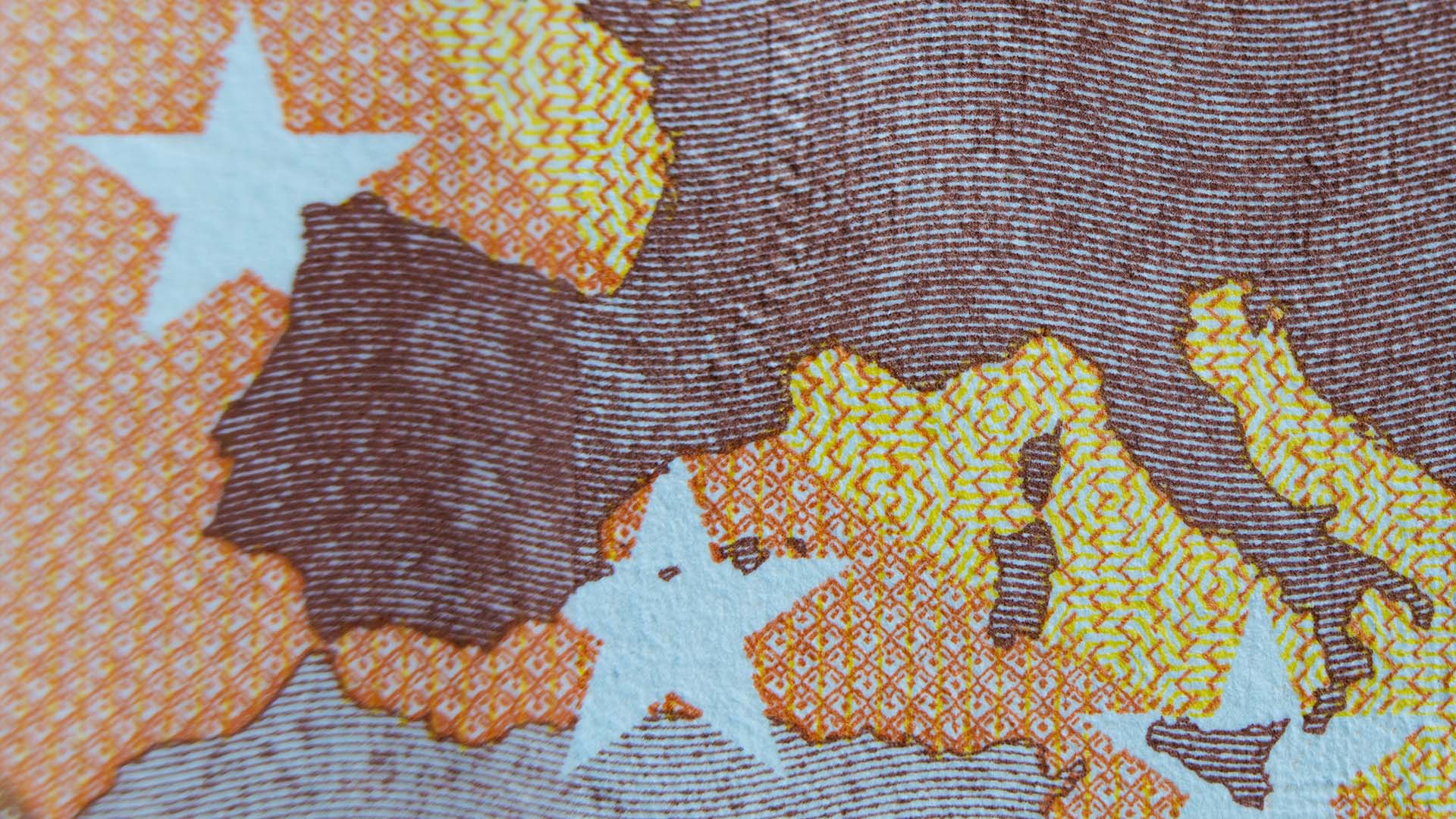 Detalle ampliado de un billete de cincuenta euros donde se resalta una parte de Europa en tonos ocre. En el fondo, se observa un patrón con líneas de colores amarillo y naranja, así como algunas estrellas de color blanco. España