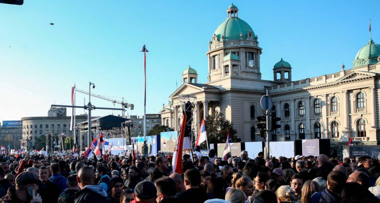Manifestación organizada por el gobierno de Serbia, el 12 de abril de 2025, bajo el lema “Asamblea popular: no entregamos Serbia”. Al fondo se ve el edificio del Parlamento de Serbia con su cúpula verde, mientras numerosas banderas serbias ondean entre la multitud bajo un cielo despejado. Serbia
