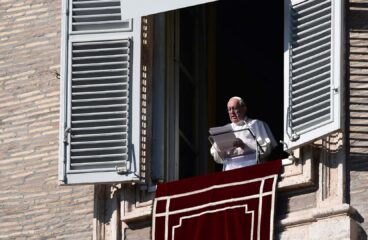 El Papa Francisco lee un discurso desde una ventana del Palacio Apostólico en el Vaticano durante el rezo del Ángelus, con una cortina roja decorativa colgando del alféizar. Vaticano