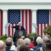 Donald Trump, desde un atril con micrófono, señala con su brazo derecho durante su alocución ante una audiencia congregada en el evento Make America Wealthy Again o “Día de la Liberación” en la Rosaleda de la Casa Blanca, el pasado 2 de abril de 2025. Detrás, cuatro banderas de EEUU cuelgan verticalmente entre los pilares de columnas.