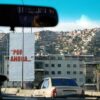 Foto de una pancarta blanca con la frase en rojo “Por ahora…”, tomada desde un coche en la autopista Caracas – La Guaira. Detrás de la pancarta, un edificio bajo de apartamentos y al fondo la imagen de un cerro o barriada popular en el oeste de la ciudad de Caracas (Venezuela). La frase fue pronunciada por Hugo Chávez Frías en su rendición ante los medios de comunicación, tras el intento de golpe de Estado en 1992.